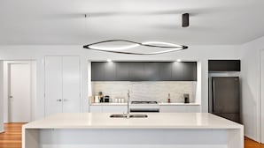 A modern kitchen with a central island, stainless steel appliances, and a minimalist design. - Luxury Large Home - LATE CHECK OUT Feb-Nov 2025 (Point Lonsdale)