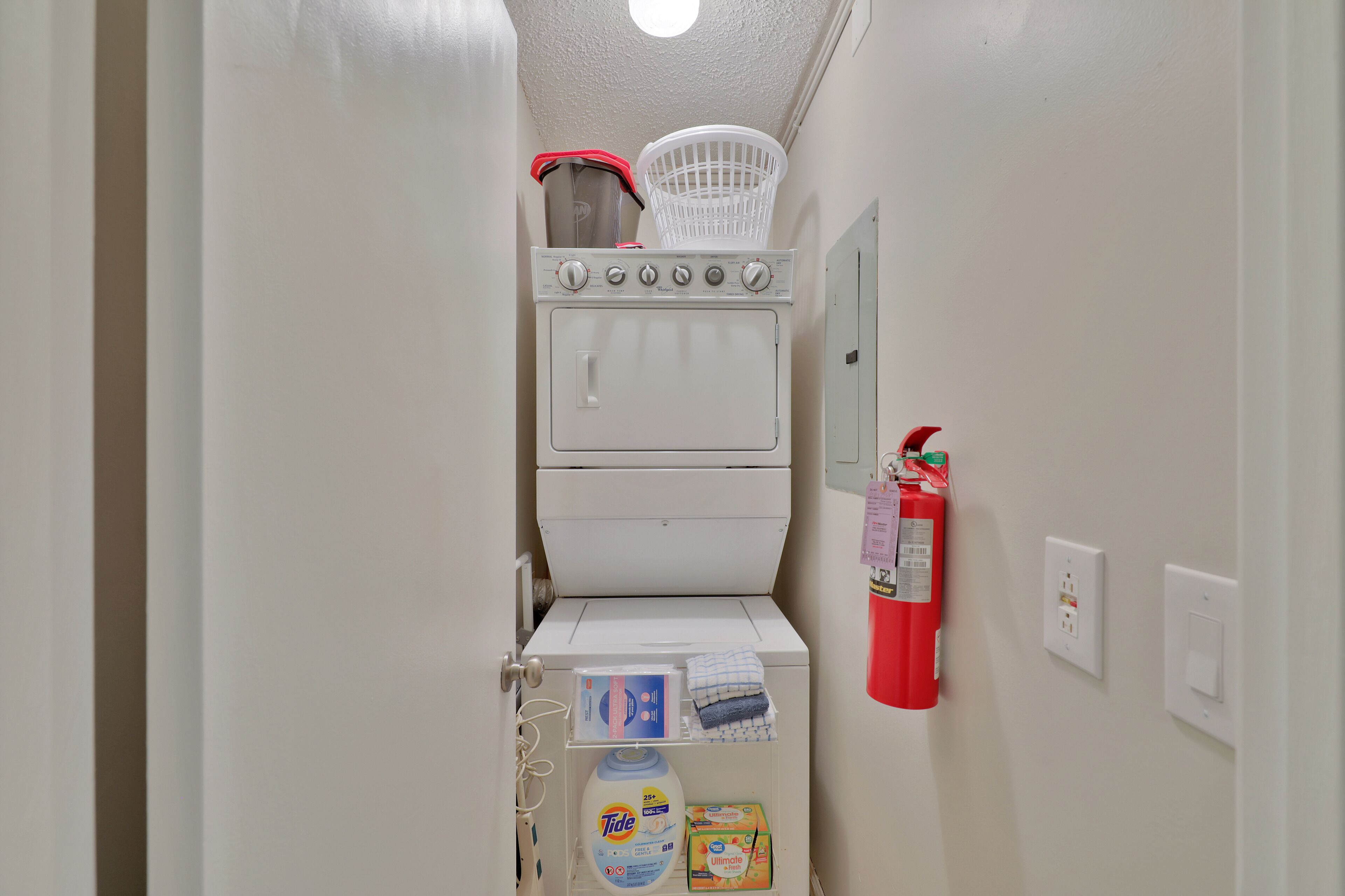 A laundry room with a stacked washer and dryer, a fire extinguisher, and laundry supplies.