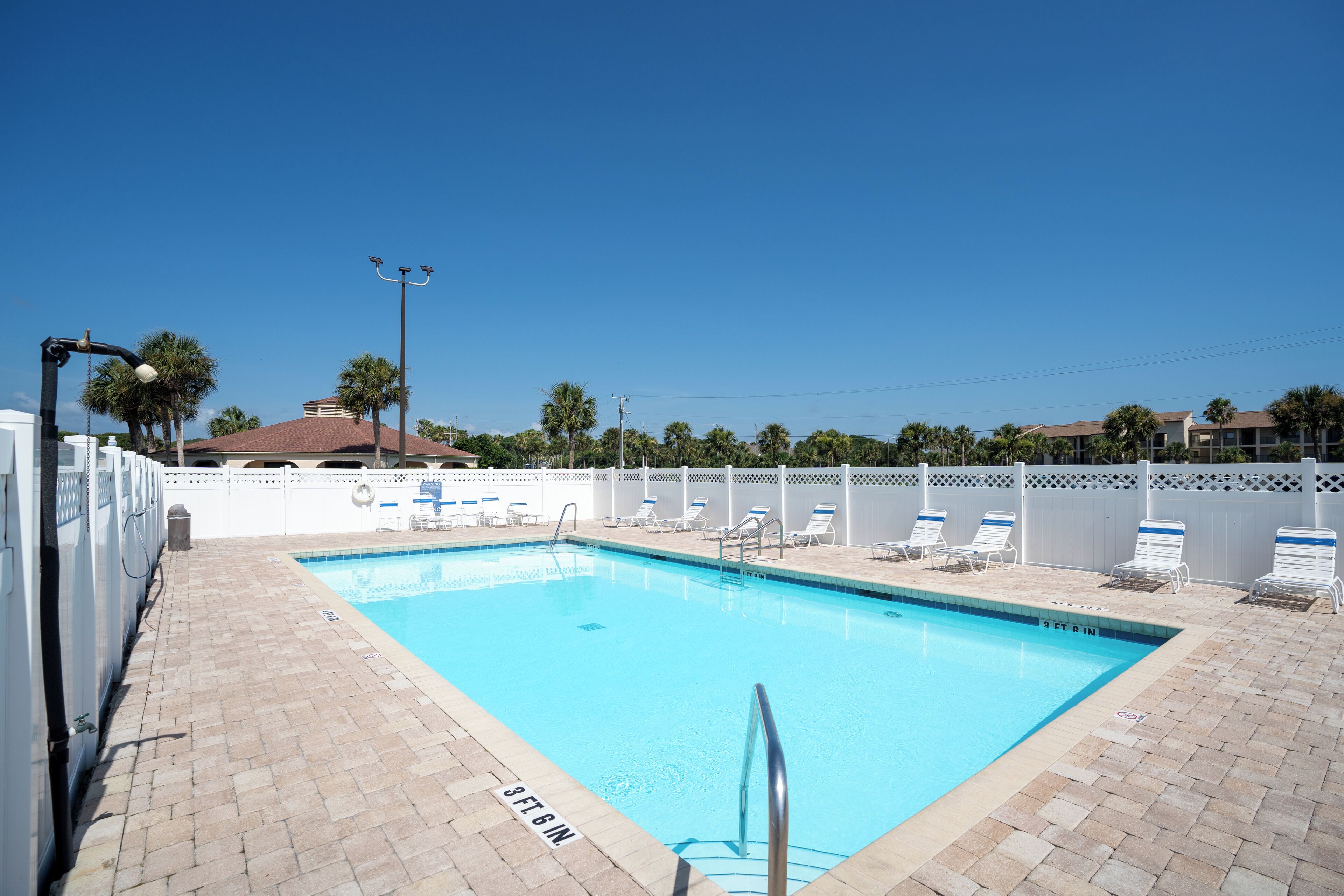 A rectangular swimming pool with a tiled deck, a metal ladder, and lounge chairs.