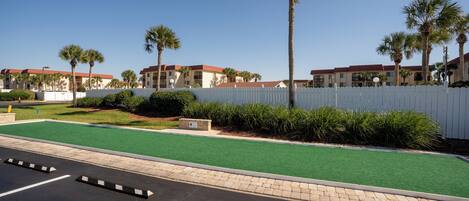 A parking lot with green artificial turf, a white picket fence, and palm trees.
