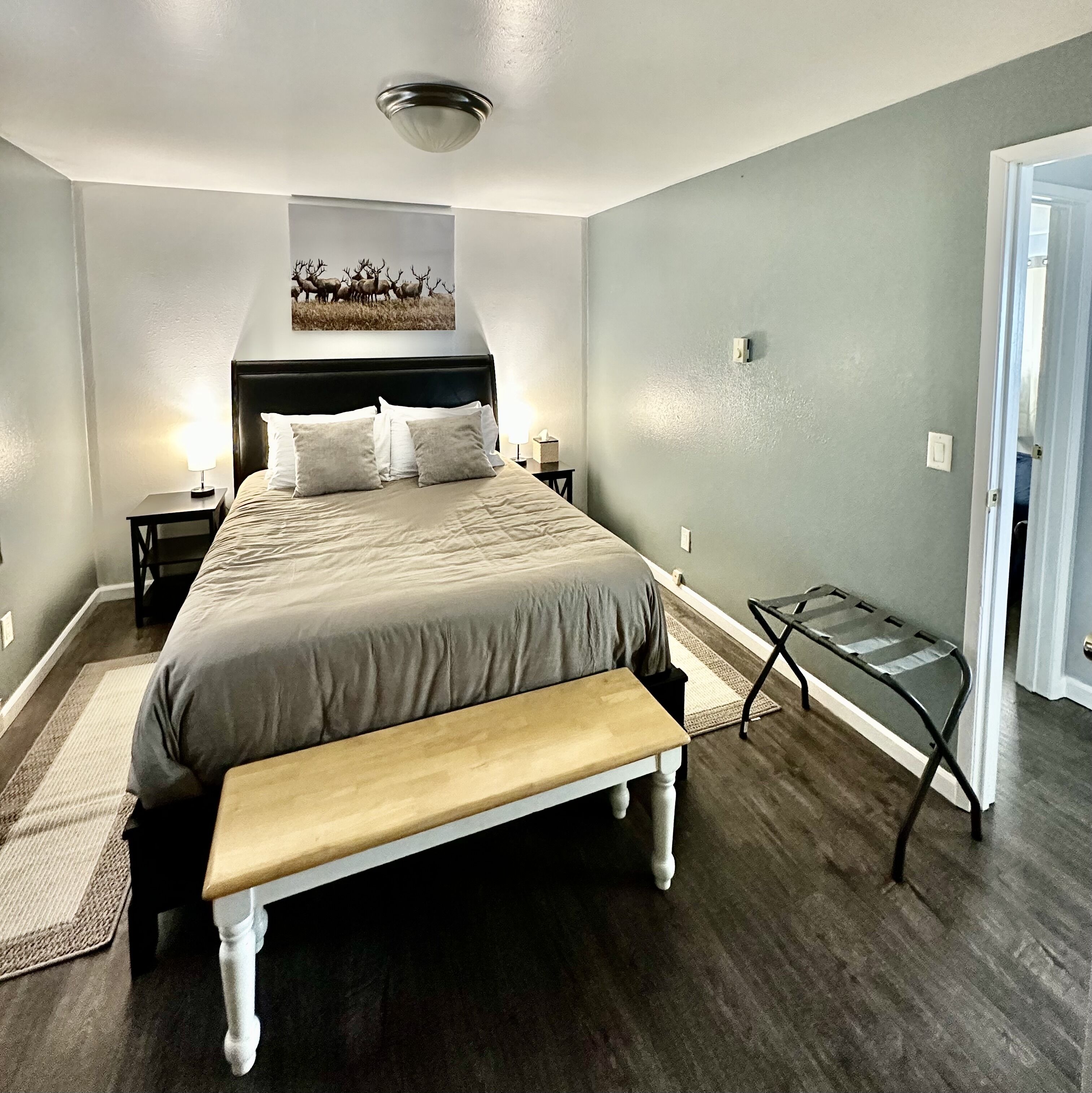 A bedroom with a bed, bedside tables, a bench, a wall-mounted light fixture, and a door.