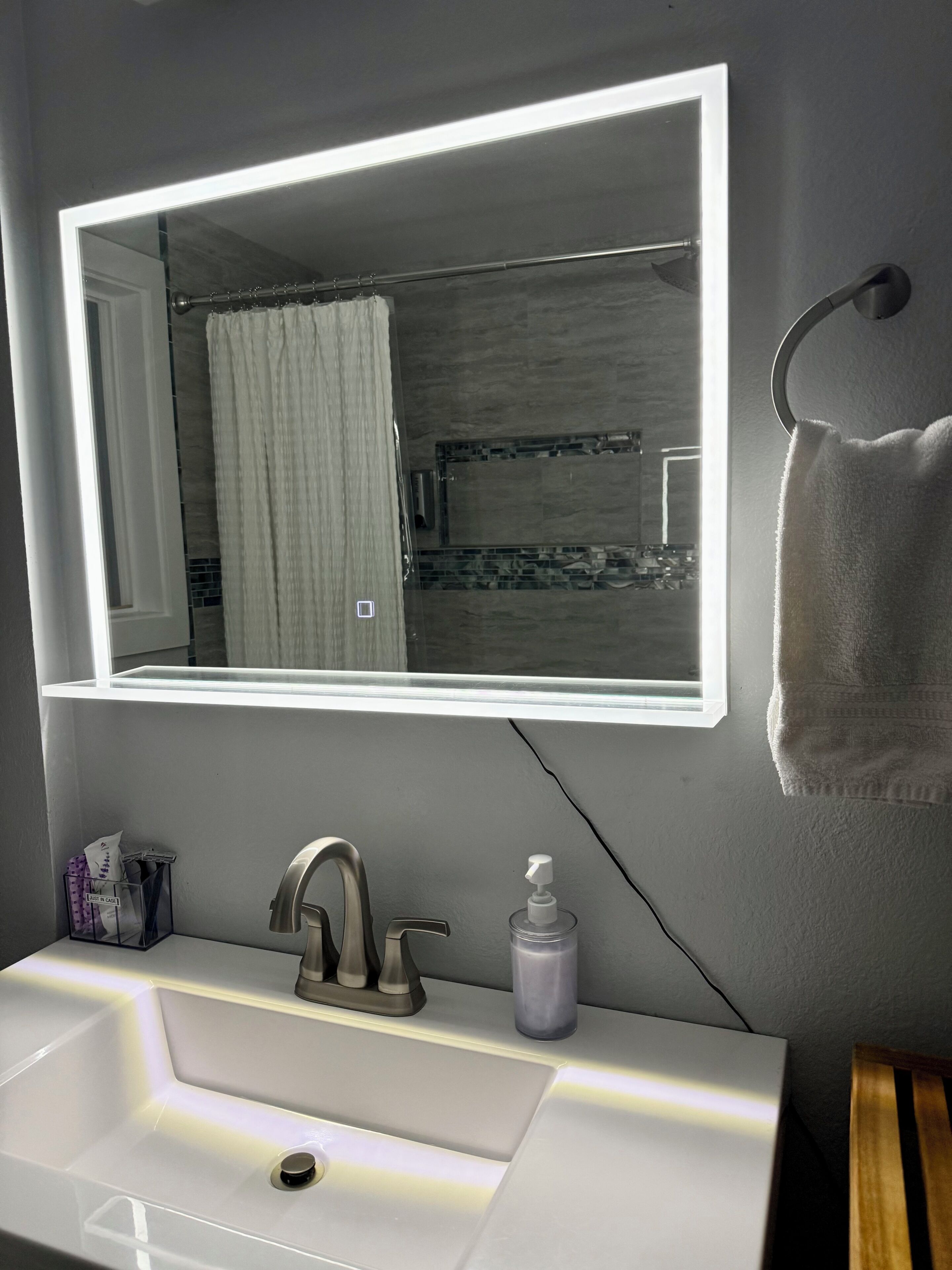 Une salle de bain avec un lavabo blanc, un miroir doté d’un éclairage à DEL, un porte-serviettes et un rideau de douche.