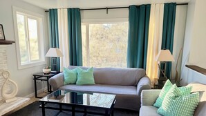Een woonkamer met een bank, twee bijzettafels met lampen, een salontafel en een raam met gordijnen.