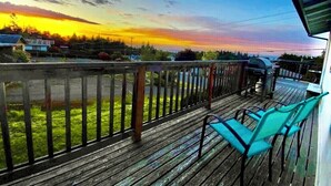 Een houten terras met een balustrade, een barbecue en twee groene stoelen.