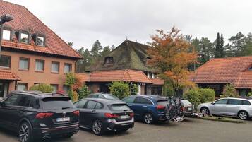 Een parkeerplaats met meerdere auto's, waaronder een zwarte SUV en een blauwe SUV, geparkeerd voor gebouwen met rode pannendaken en bakstenen gevels.