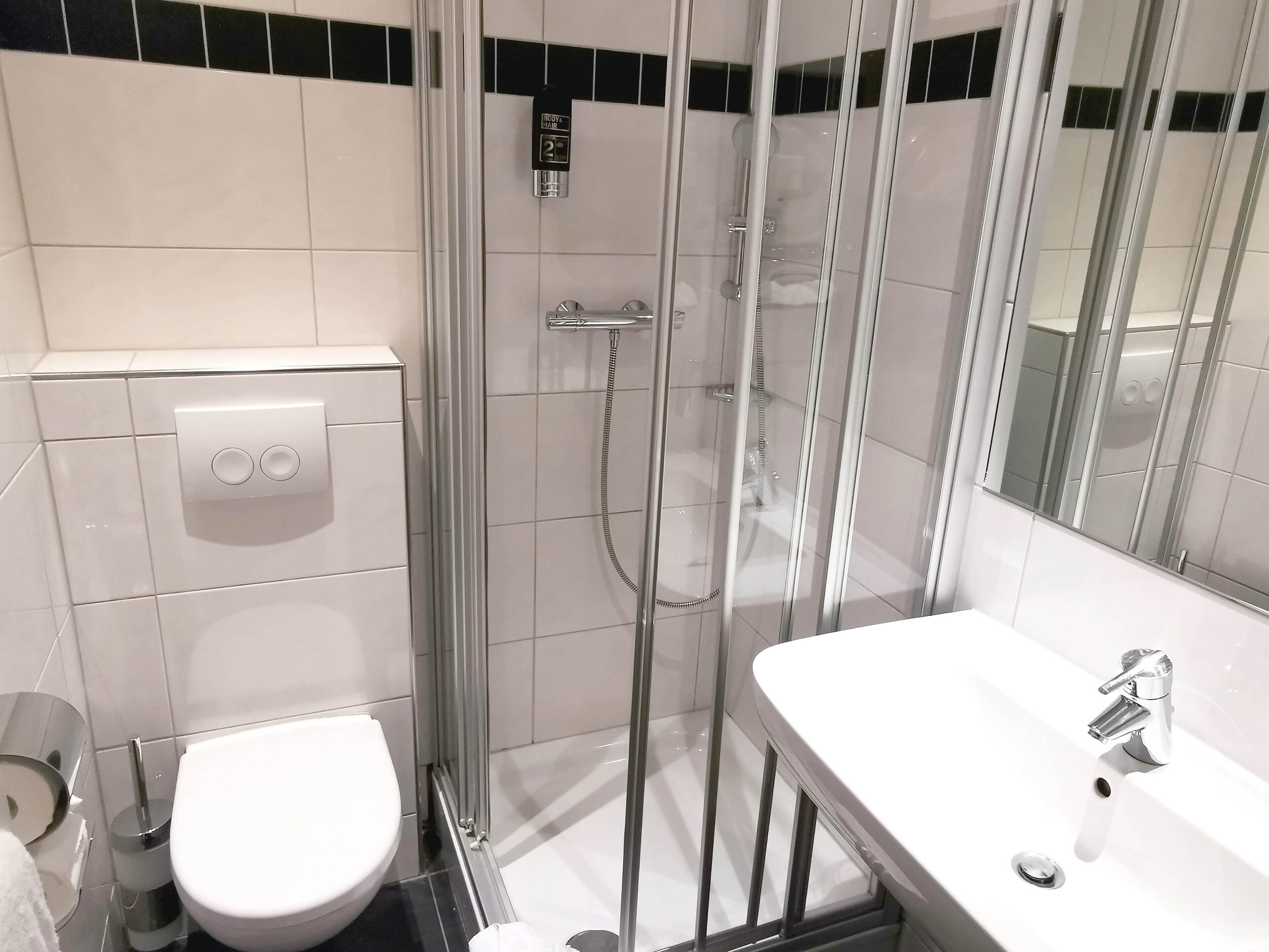 Ein modernes Badezimmer mit einer Duschkabine, einer weißen Toilette und einem Waschbecken mit Spiegel.