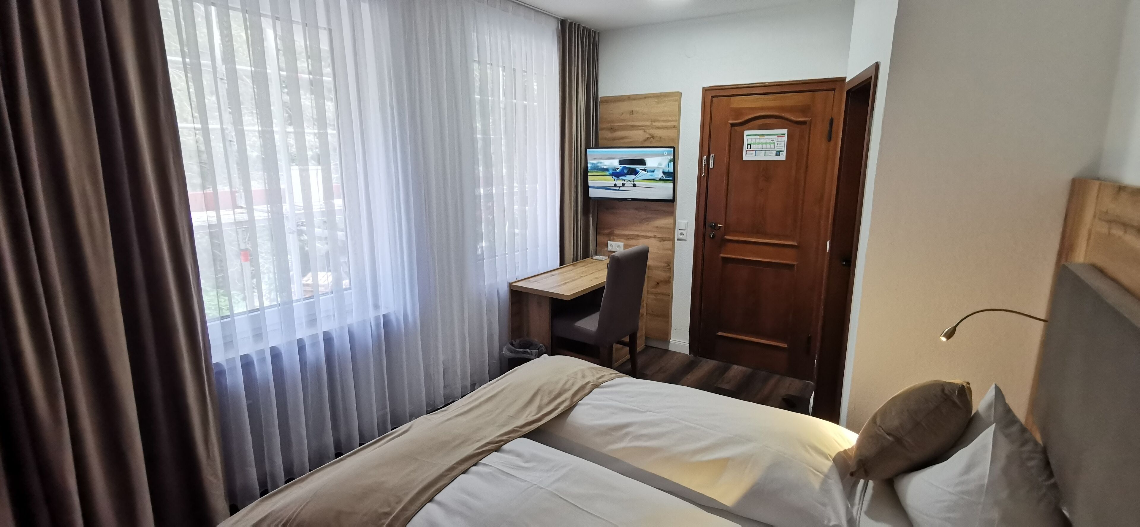 A hotel room with a bed, a desk, a TV, and a door.