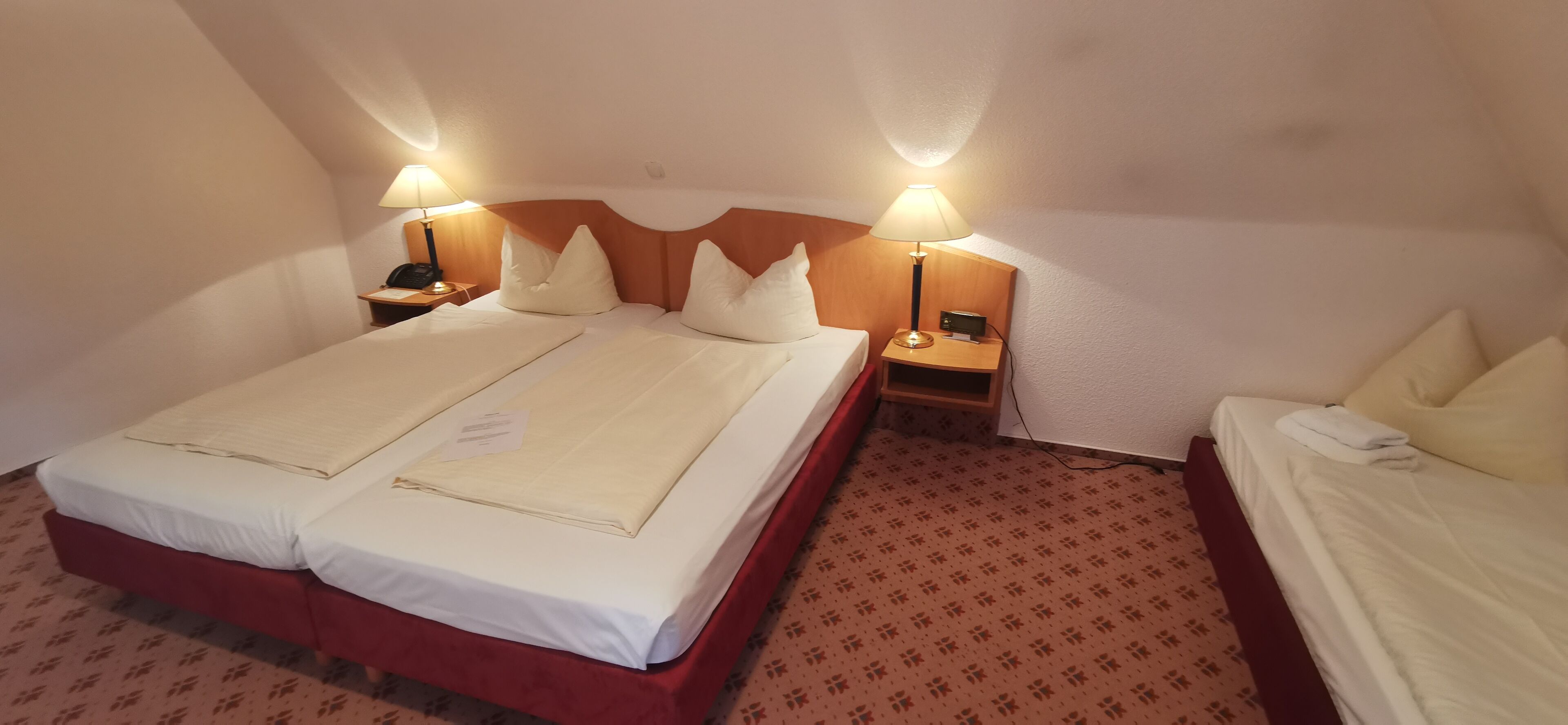 A hotel room with two beds, a red headboard, a patterned carpet, and bedside lamps.