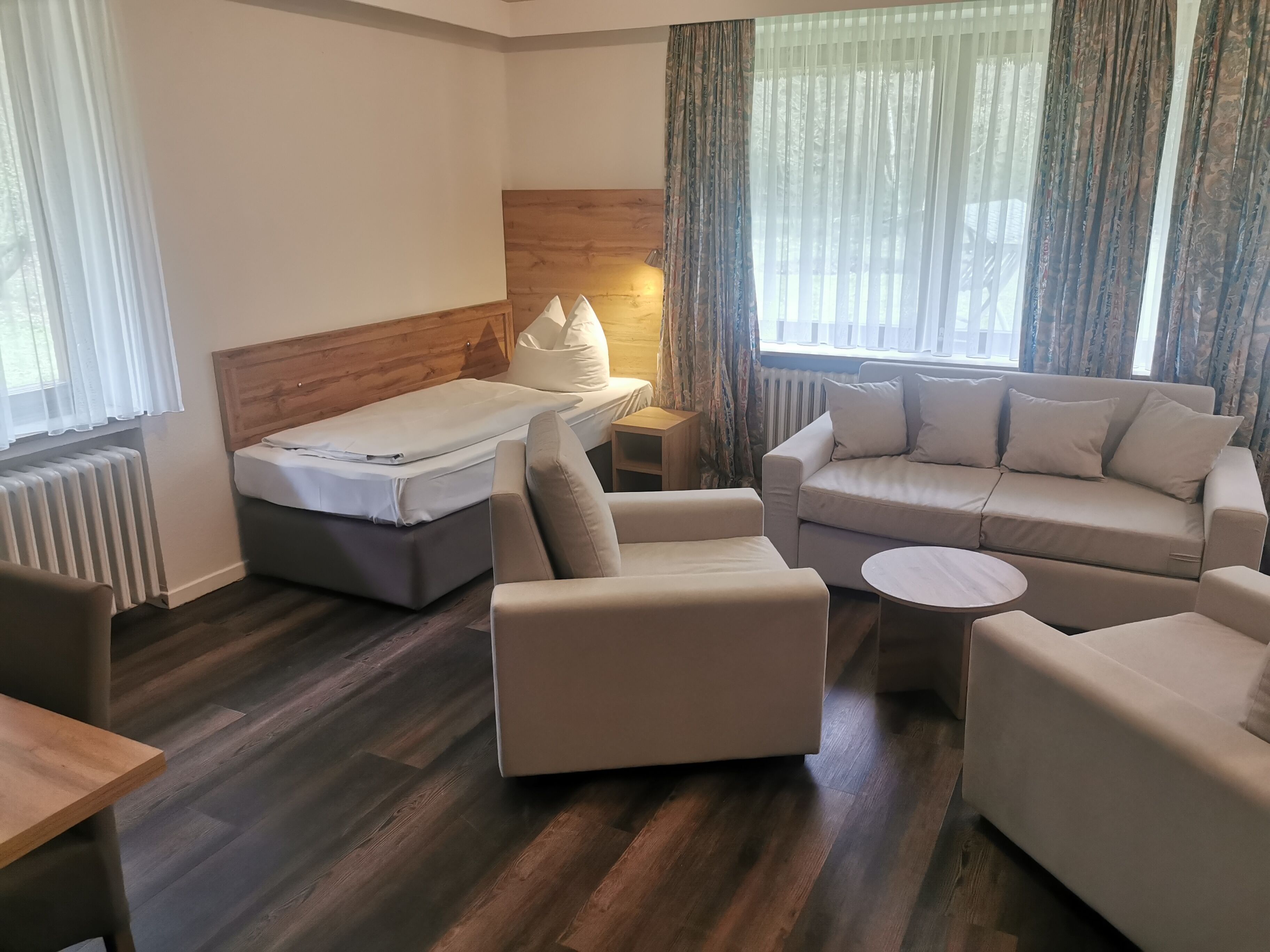 Una habitación de hotel con una cama, dos sofás, una mesita pequeña y una mesita de noche con lámpara.