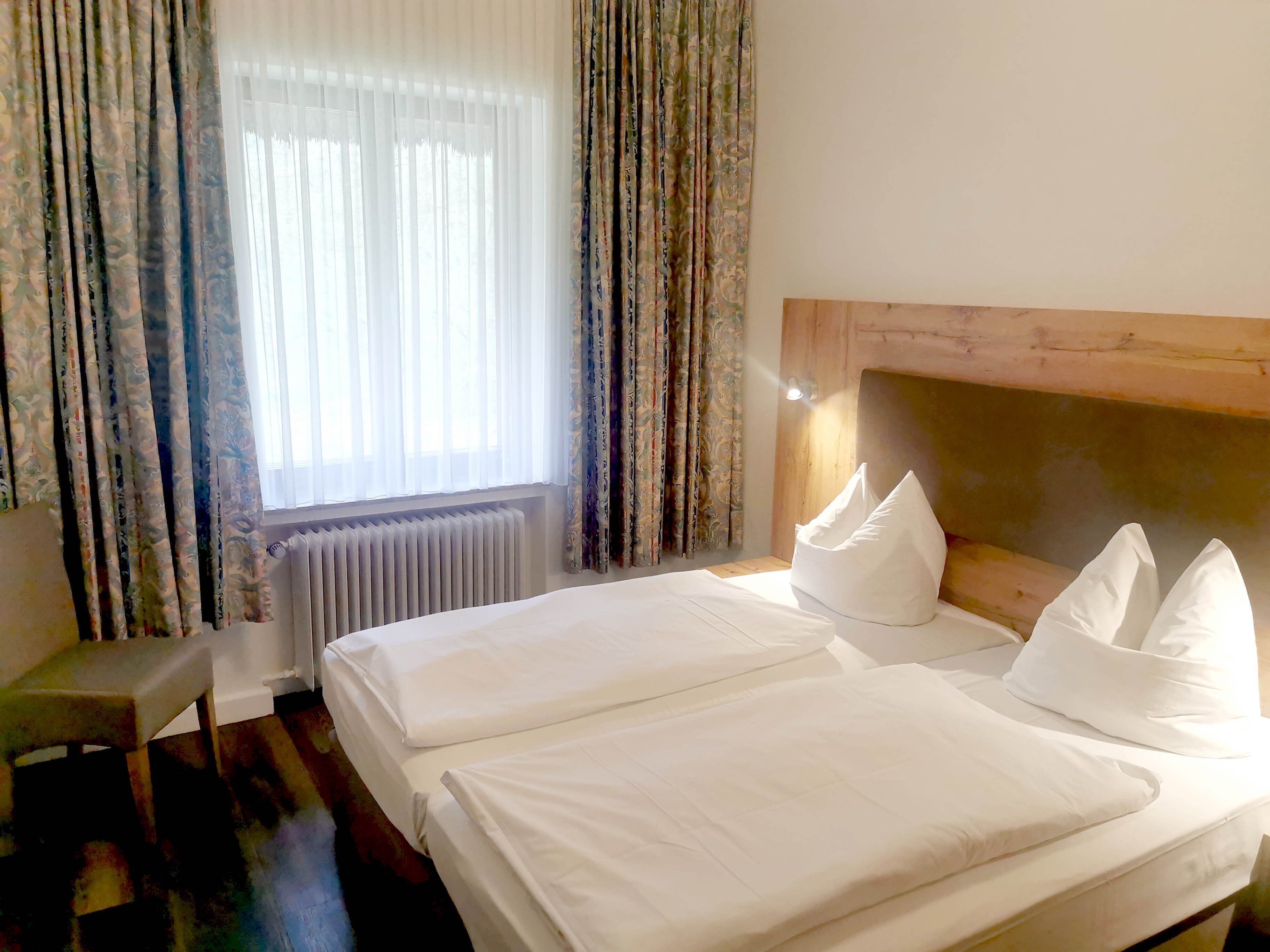 A hotel room with two beds, a wooden headboard, a radiator, and a chair.