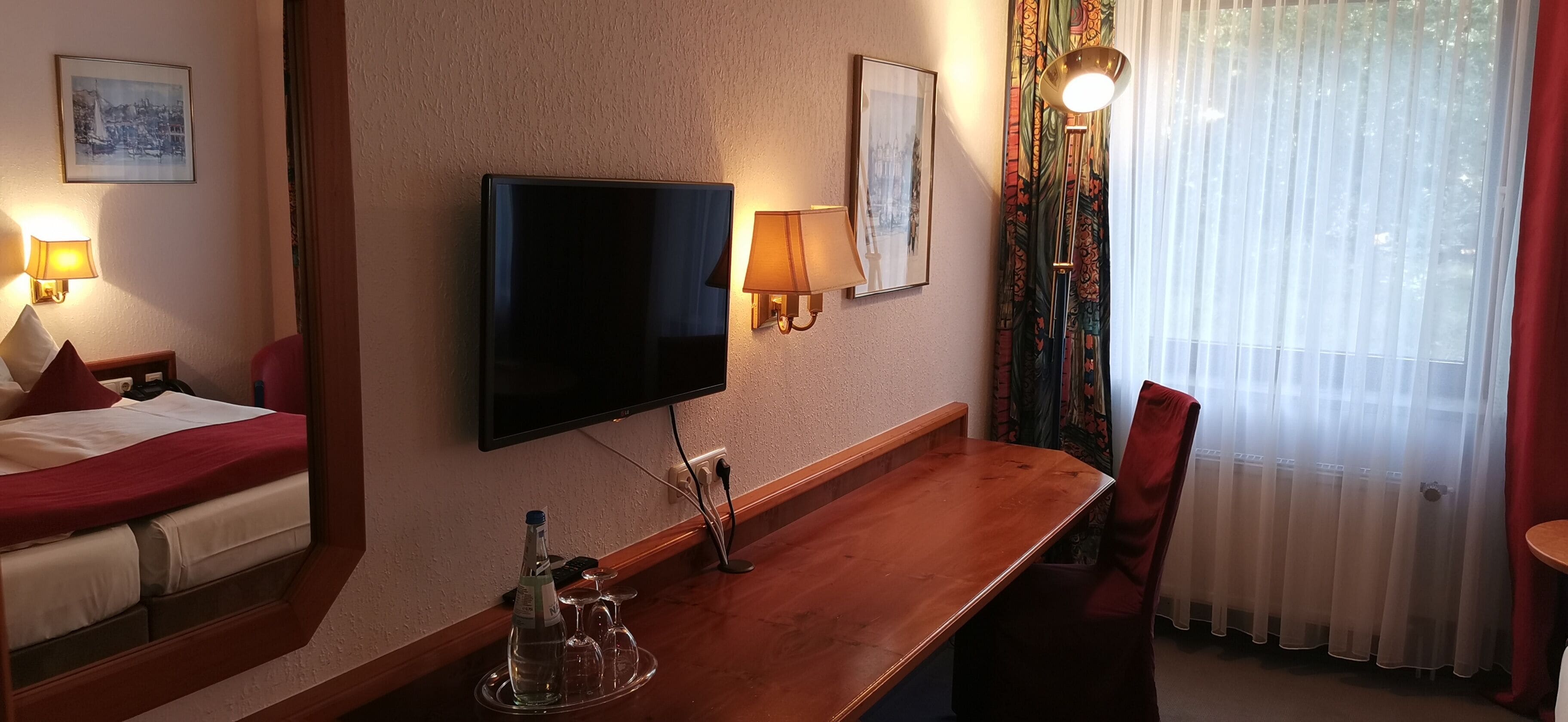 A hotel room with a bed, a TV mounted on the wall, a wooden table, and a chair.