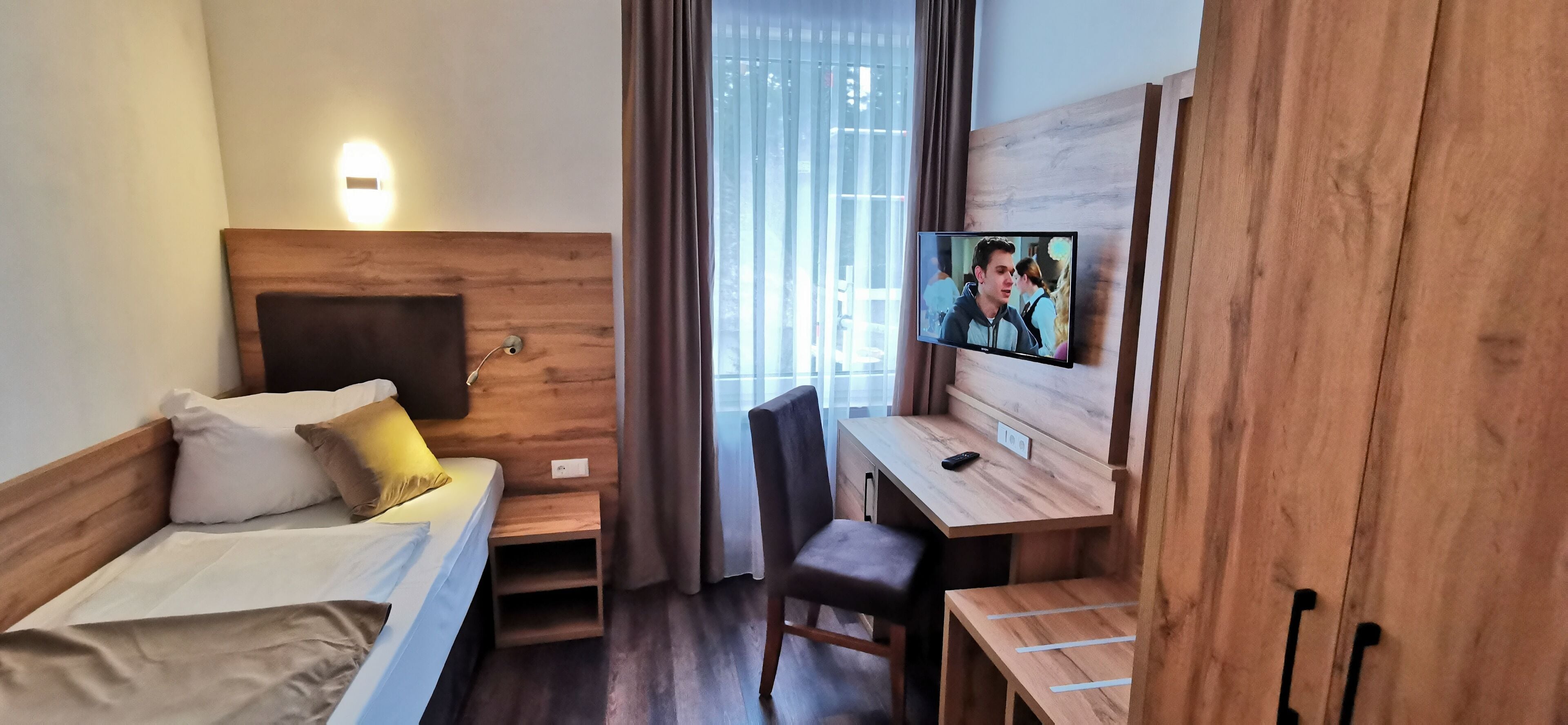 Habitación de hotel con cama, escritorio, silla, televisión y ventana con cortinas.