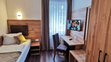 A hotel room with a bed, a desk, a chair, a TV, and a window with curtains.
