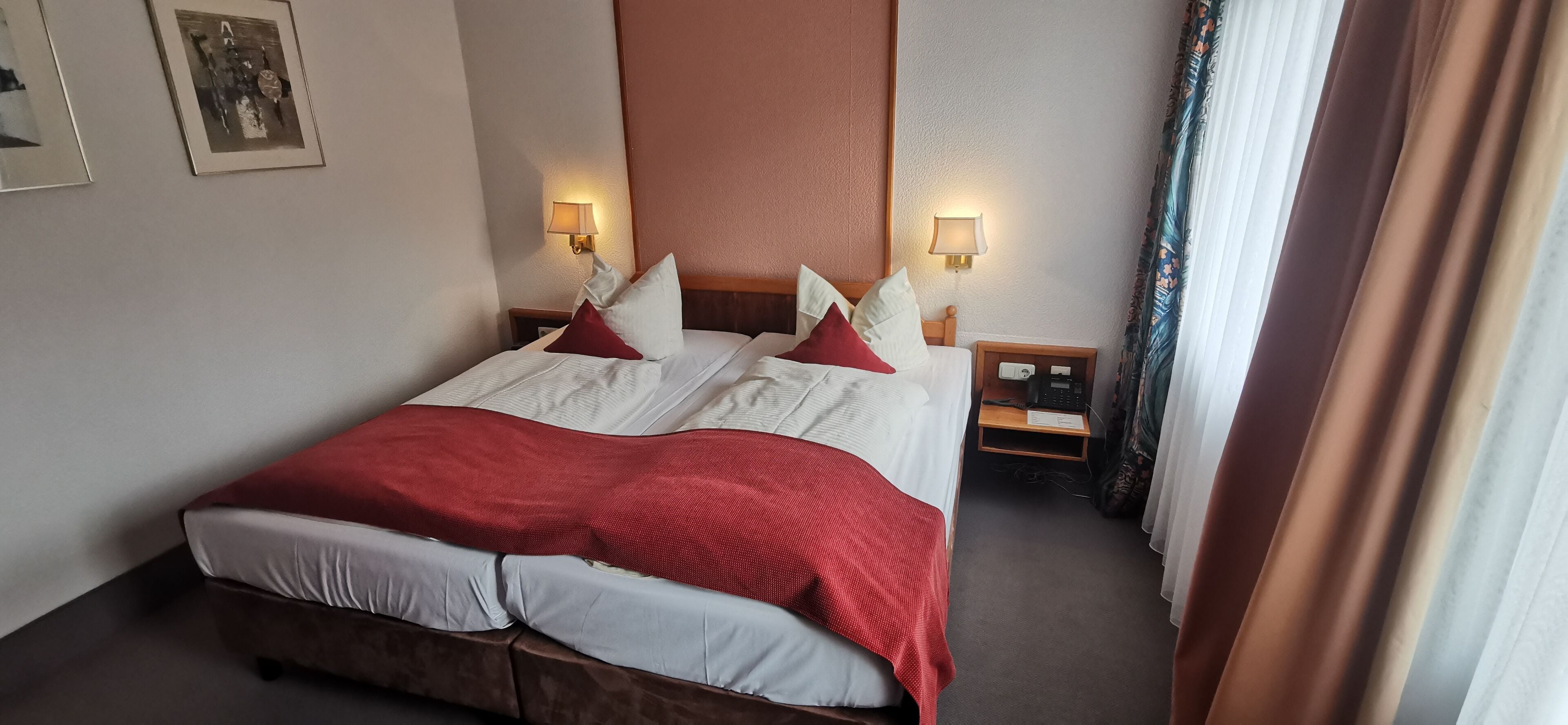A hotel room with a large bed, two bedside tables, a nightstand, and a wall-mounted lamp.