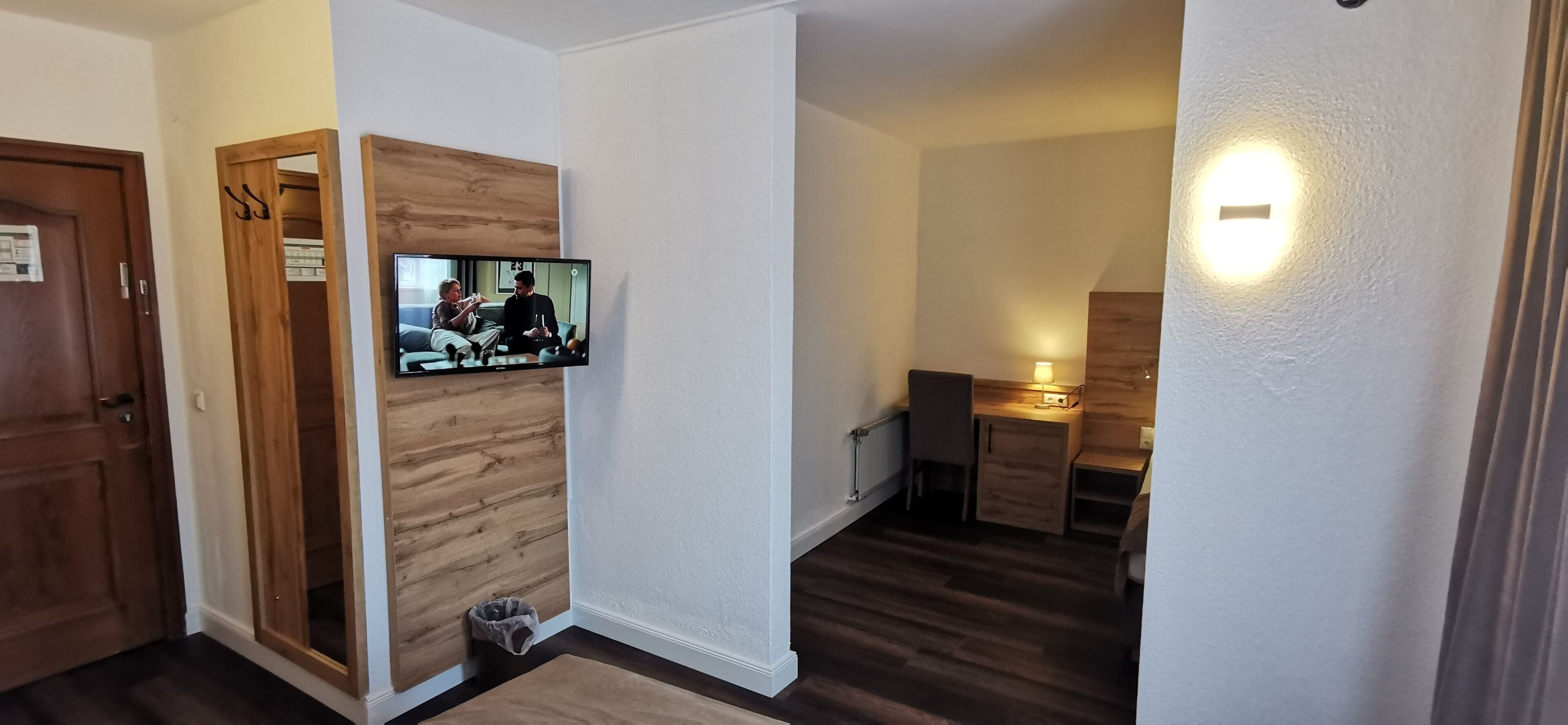 A hallway with a wooden wall, a television mounted on it, and a small trash bin.