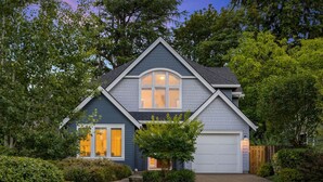 A two-story house with a garage, surrounded by trees and shrubs.