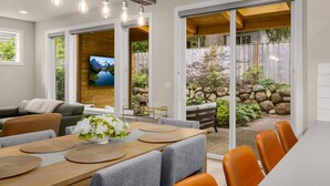 A modern dining area with a wooden table, grey upholstered chairs, and a TV mounted on a wooden wall.