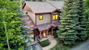 A two-story house with a porch, surrounded by trees and a mountainous landscape.