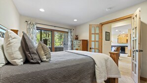 A bedroom with a large bed, a dresser, and a view of the kitchen through an open door.