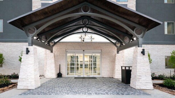 A building entrance with a stone facade, a metal roof, and a glass door. - Outdoor Pool. Free Breakfast. Cozy Queen Studio. (Lake Charles)
