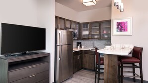 A modern kitchen with a built-in TV, stainless steel appliances, and a dining area with a white table and red chairs. - Outdoor Pool. Free Breakfast. Cozy Queen Studio. (Lake Charles)