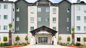 A Staybridge Suites hotel with a modern architectural design, featuring a central entrance with a covered walkway, multiple floors, and a symmetrical facade. - Outdoor Pool. Free Breakfast. Cozy Queen Studio. (Lake Charles)