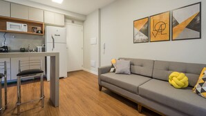 Een compacte woonruimte met een kitchenette, een bank met decoratieve kussens en abstracte wanddecoratie.