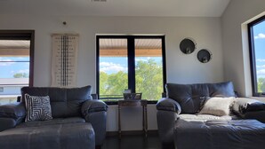 Ein modernes Wohnzimmer mit zwei Ledersofas, einem Couchtisch und Blick auf Bäume durch große Fenster.