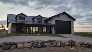 Ein modernes, zweistöckiges Haus mit großer Garage, einer Steinsäule im Vorgarten und einer grünen Landschaft.