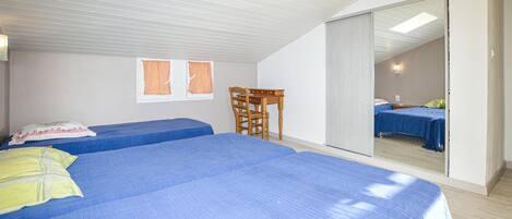 Quarto com duas camas, uma cadeira de madeira, uma mesinha e uma porta de vidro deslizante para outro cômodo.