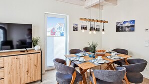 Zona pranzo moderna con tavolo in legno, sedie rivestite in grigio e televisore su un mobile in legno.