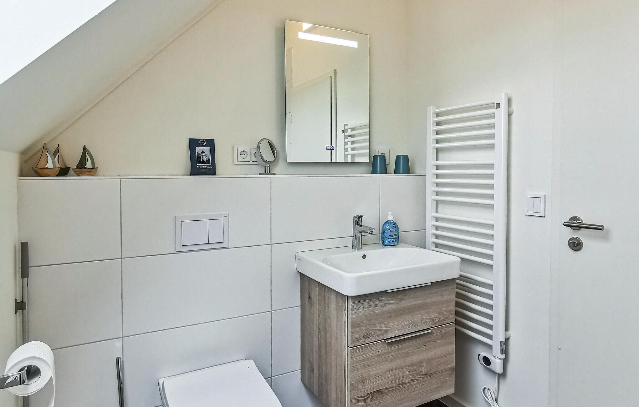 A modern bathroom with a white vanity, a mirror, a towel rack, and a toilet.