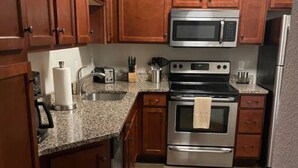 A compact kitchen with wooden cabinets, a microwave, a stove, and a sink. - Heart of Downtown 1 BR/1 BA - Hidden Gem (Norfolk)