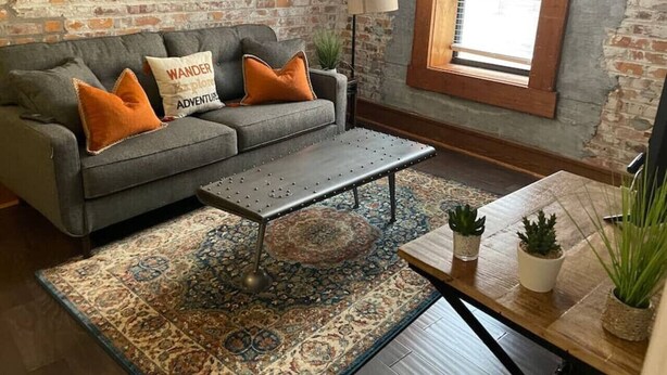 A cozy living room with a gray sofa, orange cushions, a metal coffee table, and a patterned rug. - Heart of Downtown 1 BR/1 BA - Hidden Gem (Norfolk)