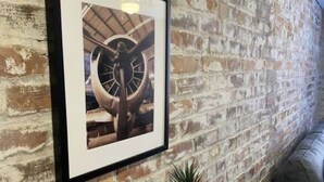 A framed picture of a ship's wheel on a brick wall, a small potted plant on a wooden table, and a gray couch. - Heart of Downtown 1 BR/1 BA - Hidden Gem (Norfolk)