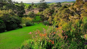 A lush garden with a variety of plants and trees, a well-maintained lawn, and a bench in the background. - Balcony river views and great value (Haruru)
