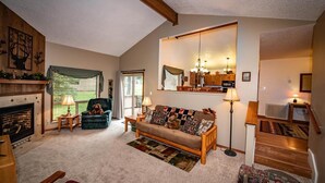 Una sala de estar acogedora con chimenea, un sofá, un sillón y una escalera que sube a otro nivel.