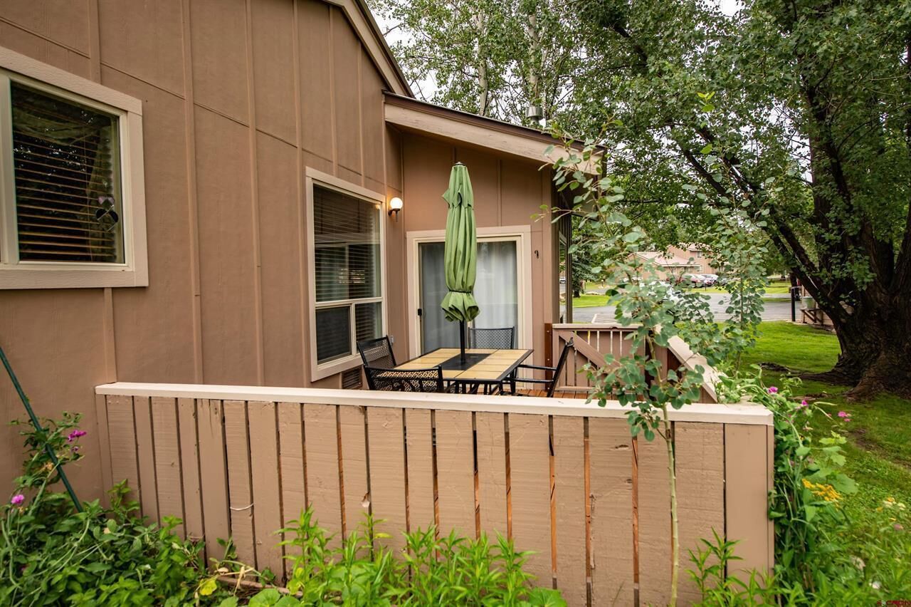 Une maison dotée d’un patio comprenant une table et des chaises, un parasol vert et une clôture en bois.
