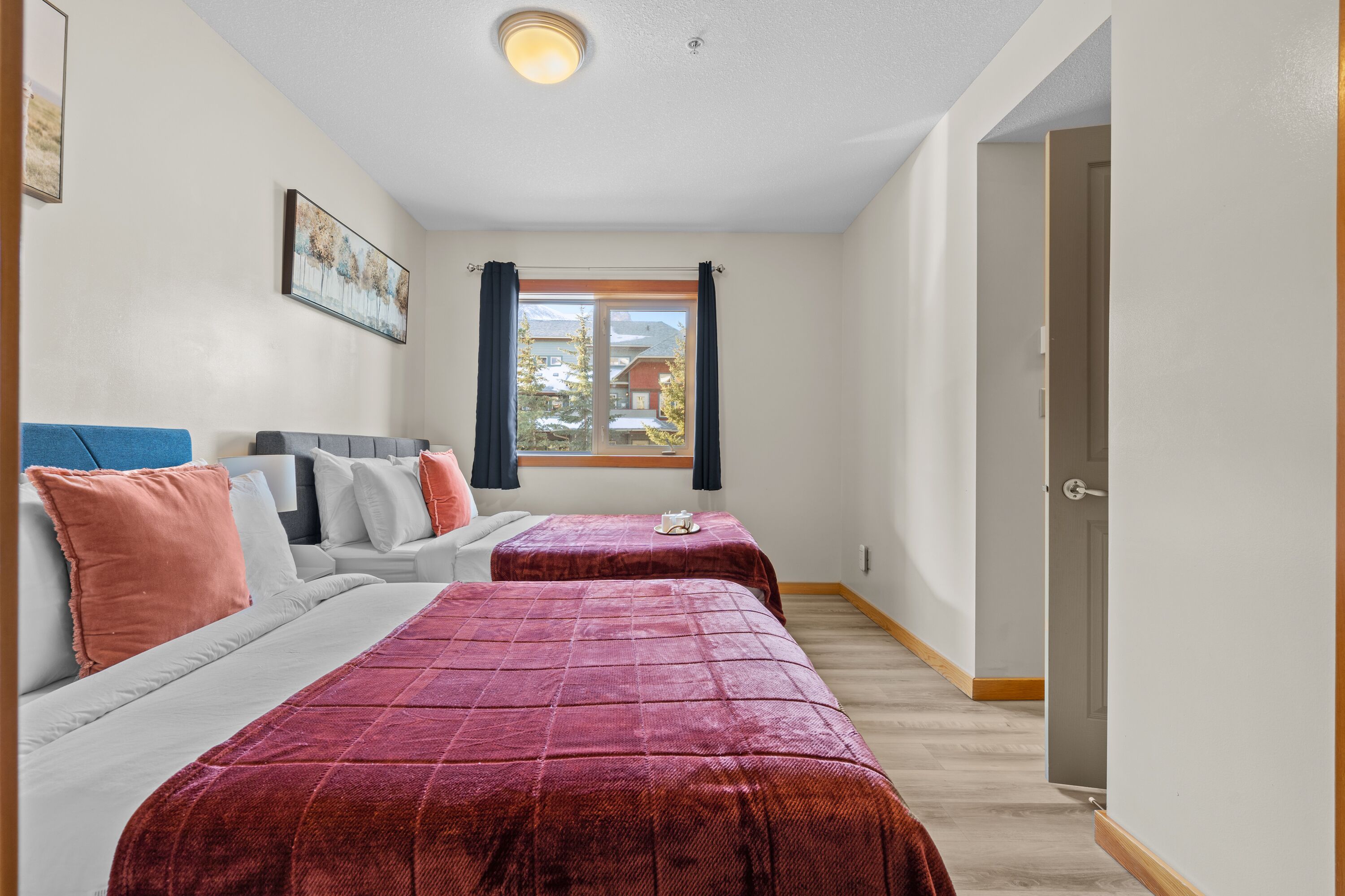 A room with two beds, a sofa, a window with curtains, and a door.