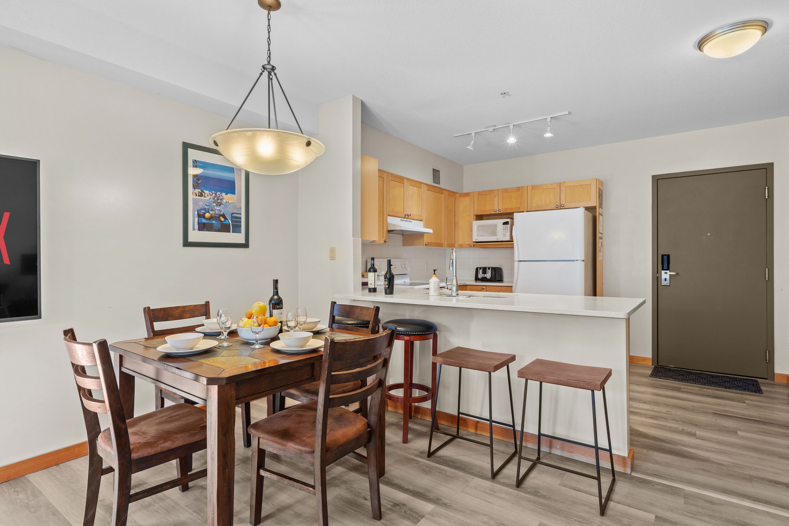 A modern kitchen with wooden cabinets, a white countertop, and a built-in microwave. There is a dining area with a wooden table and chairs.