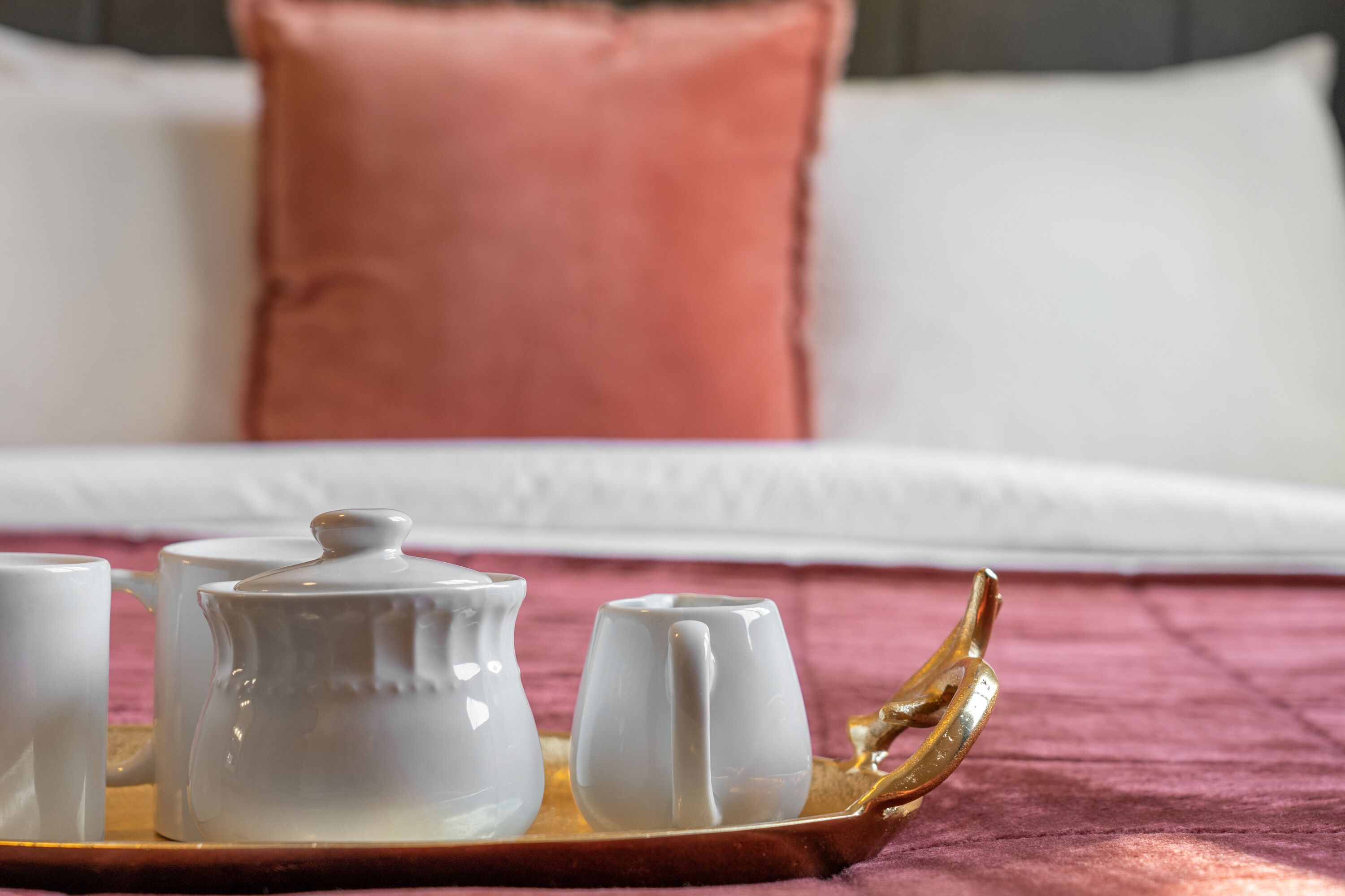 A tray with a teapot and cups on a bed with a pink pillow.