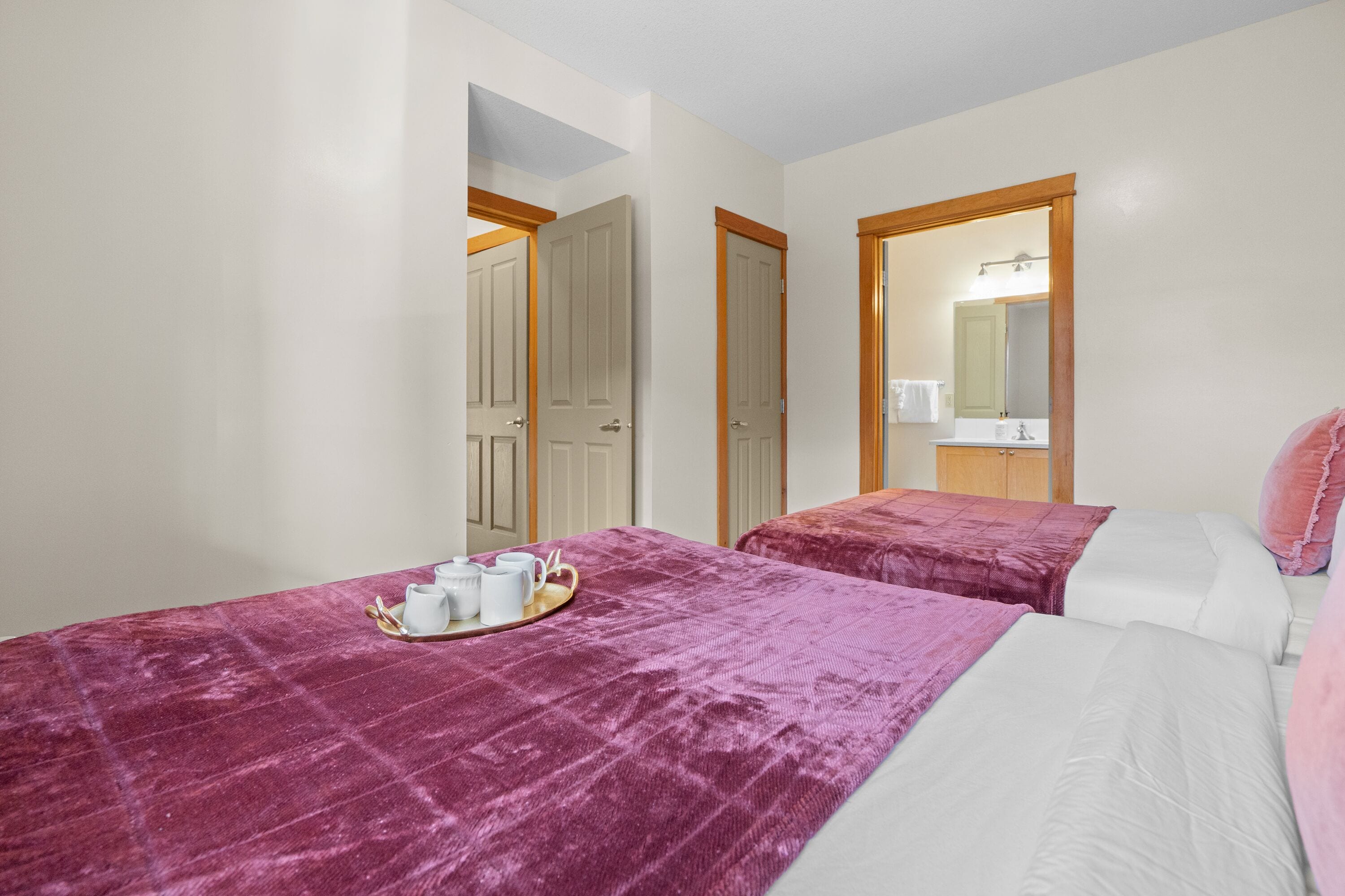 Ein Hotelzimmer mit zwei Betten, einem Badezimmer mit Spiegel und einem Tablett mit Tassen und Teekanne auf dem Bett.