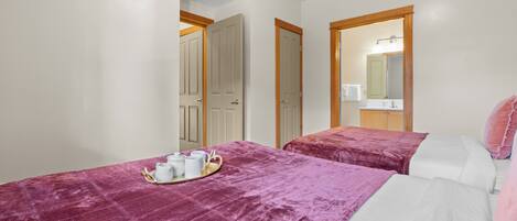 A hotel room with two beds, a bathroom with a mirror, and a tray with cups and a teapot on the bed.
