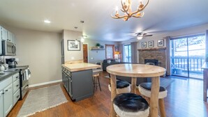 Una cocina moderna con una isla central, un comedor con taburetes, una chimenea y un amplio ventanal con vistas.