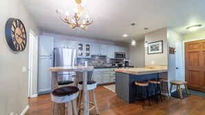 Una cocina moderna con armarios azul claro, una isla central con taburetes, una lámpara de araña y un reloj grande en la pared.