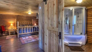 Interior de una cabaña con paredes de madera, una cama, un banco, una sauna y una puerta.
