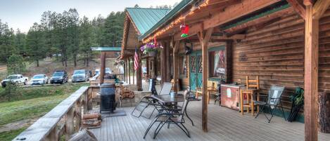 A wooden cabin with a deck, outdoor seating, and a view of parked cars and trees.