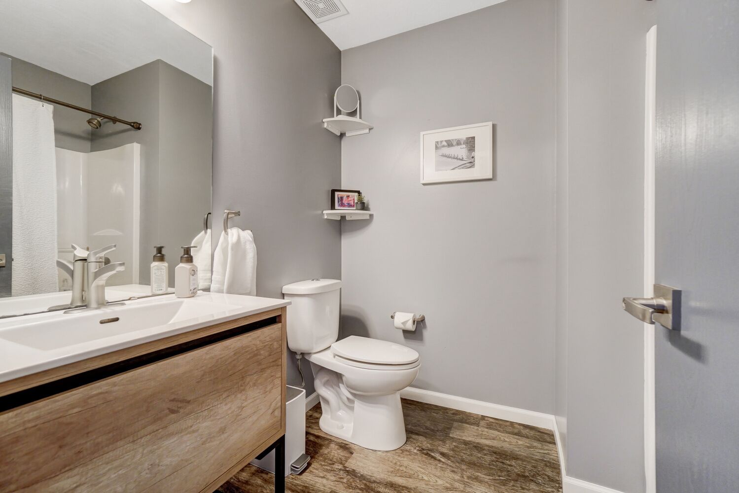 A modern bathroom with a wooden vanity, white fixtures, and a gray wall.