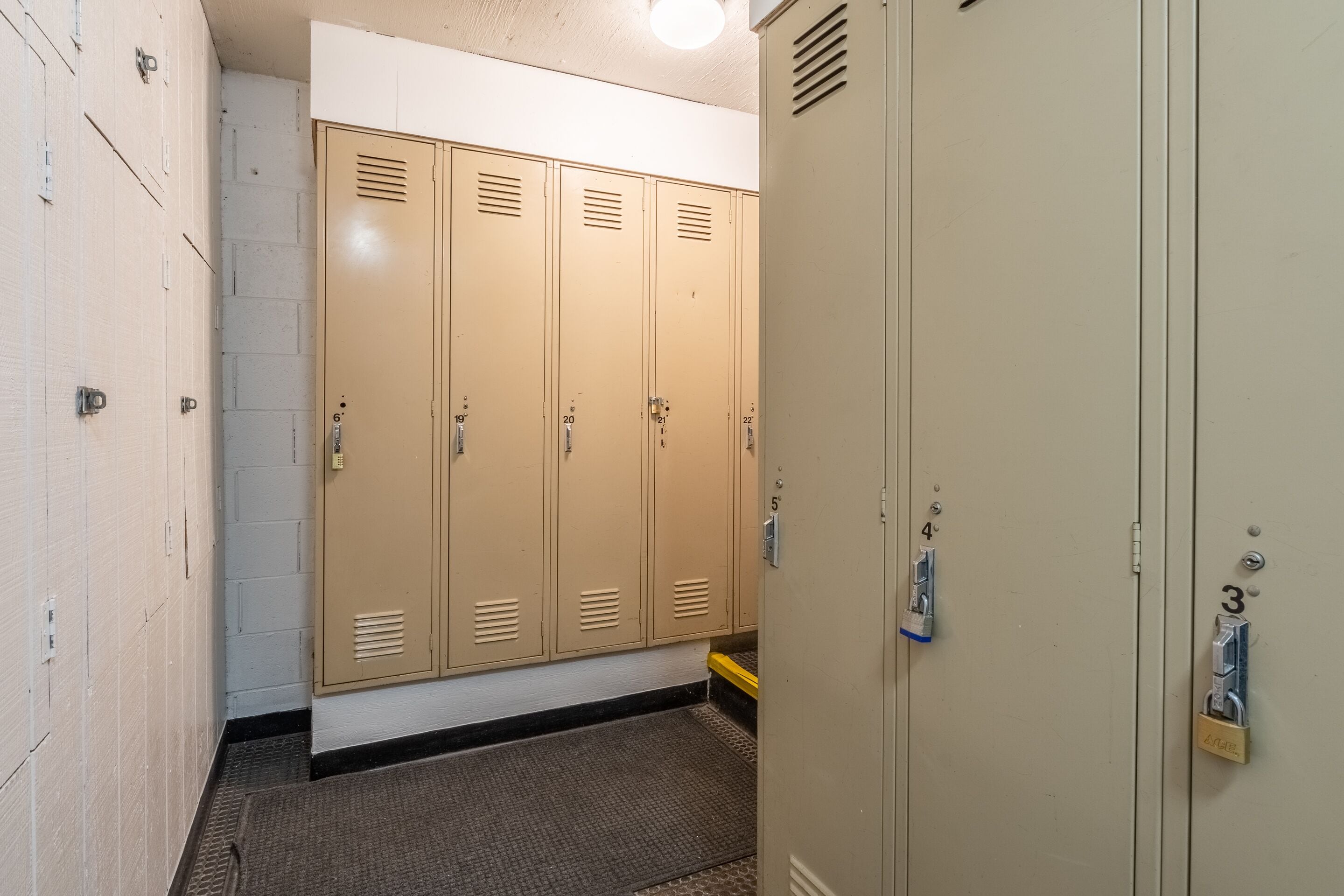 A hallway with beige lockers, numbered 3 to 20, and a door with a lock and a keyhole.