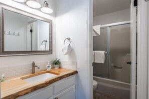 Un baño con tocador de madera, un espejo grande, un lavabo, una ducha y un inodoro.